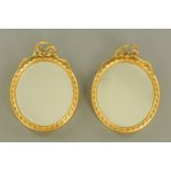 A pair of late 19th/early 20th century oval gilt framed mirrors, each with ribbon surmount.