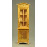 A standing corner cabinet, gold painted, the upper section with arched pediment above a glazed door,