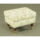 An upholstered footstool, modern, raised on turned legs with brass castors. Length 58 cm.