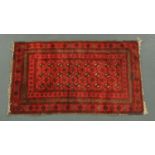 A red ground Persian rug, with geometric medallions and knotted fringed ends. 140 cm x 89 cm.