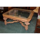 Large square glass top coffee table with canted angles and heavily carved legs,