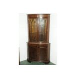 Mahogany bowfronted freestanding corner cupboard with dentil cornice above a pair of glazed doors