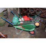 A modern green plastic wheelbarrow with metal frame, together with a variety of watering cans,