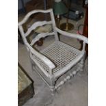 A white painted ladder back low armchair with caned seat, seat height 28.