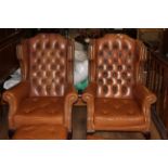 A pair of studded and deep buttoned winged Chesterfield armchairs in tan leather,