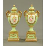 A pair of Noritake handpainted lidded urns on stands, with green ground and heightened with gilding,
