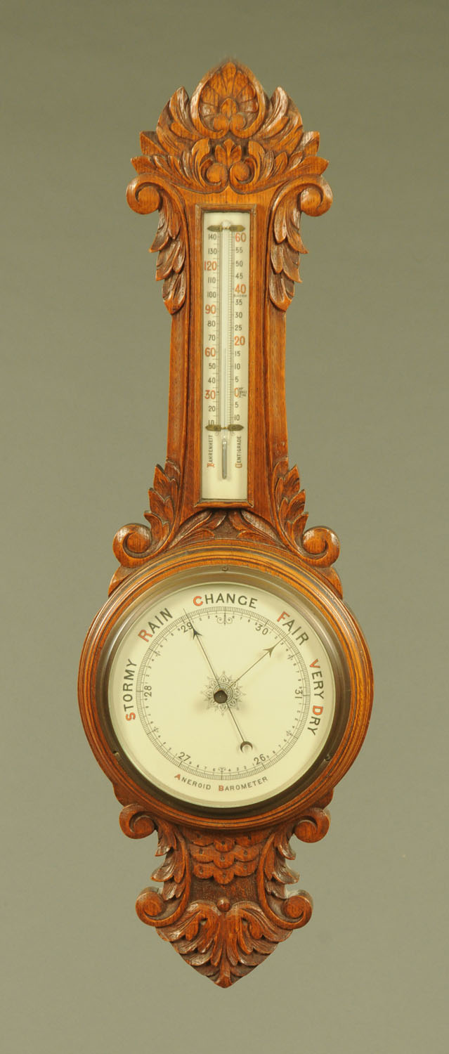 An early 20th century carved oak Aneroid barometer, with ceramic dial and scale. 81 cm.