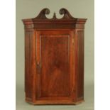 A George III mahogany corner cupboard, with swans neck pediment with carved rose terminals,