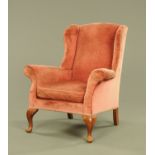 A wing easy chair in the Queen Anne style upholstered in pink velvet type material and raised on