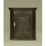 A small oak hanging corner cupboard, with carved panelled door opening to a shaped shelf.