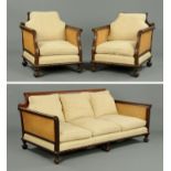 An early 20th century mahogany three piece bergere lounge suite, double caned with scroll arms,
