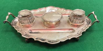 A George V silver desk stand of shaped oval form with pie crust edge and scroll handles,