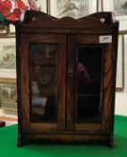 A circa 1900 oak smoker's cabinet with two glazed doors enclosing two drawers and three-section