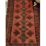 A Shirvan rug with a repeating medallion decoration on a red ground within a scrolling foliate