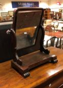 An early Victorian figured mahogany framed dressing mirror on scroll supports to the platform base