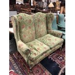 An early 20th Century two seater wingback sofa with a shaped back raised on squat cabriole legs to