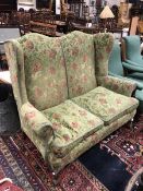 An early 20th Century two seater wingback sofa with a shaped back raised on squat cabriole legs to