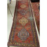 A Persian runner with repeating medallion decoration on a red ground approx.