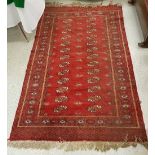 A Bokhara rug, the central panel set with two rows of elephant foot medallions on a red ground,