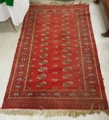 A Bokhara rug, the central panel set with two rows of elephant foot medallions on a red ground,