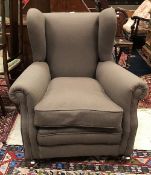 A circa 1900 upholstered wing back scroll armchair on turned feet to castors