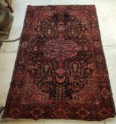 A Persian rug, the central panel set with floral decorated medallion on a dark blue and pink ground,