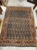 A Kashan rug, the central panel set with repeating hook motifs on a dark ground,