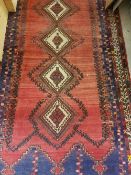 A Persian rug with five repeating lozenge shaped medallions on a red ground within a blue and white