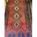 A Persian rug with five repeating lozenge shaped medallions on a red ground within a blue and white