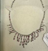 A white metal necklace set with small red stones