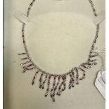 A white metal necklace set with small red stones