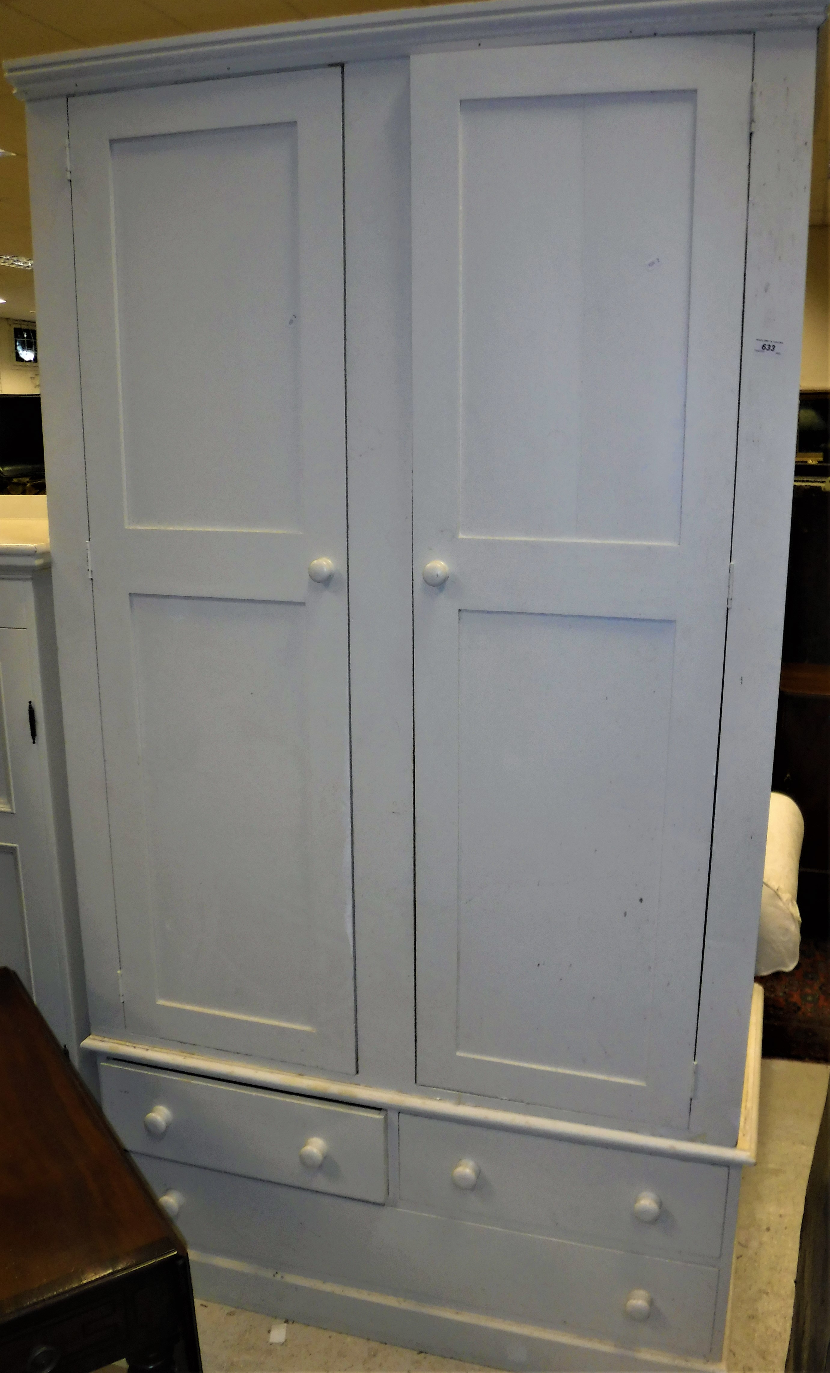 A white painted pine wardrobe with moulded cornice over two cupboard doors enclosing a shelf and