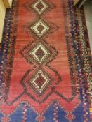 A Persian rug with five repeating lozenge shaped medallions on a red ground within a blue and white