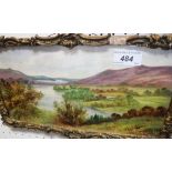 A framed painted ceramic tile of a landscape overlooking some lakes,