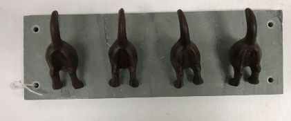 A set of four modern cast iron dog rear end coat hooks on a slate mount