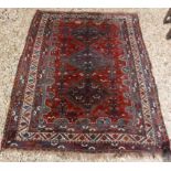 A Shiraz tribal carpet with three repeating lozenge medallions on a red ground with all over bird