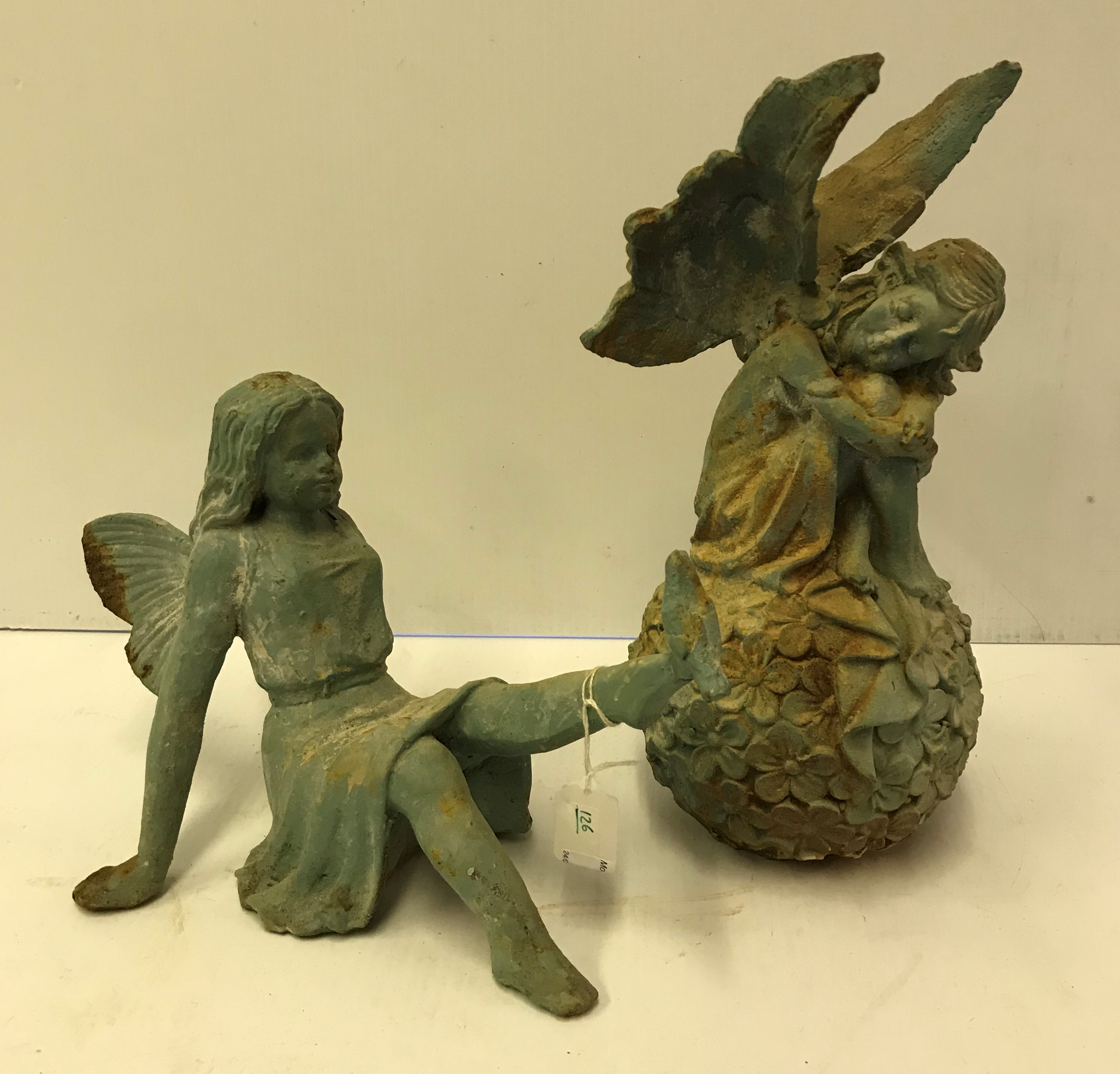 A verdigris patinated figure of an angel sat upon a flower ball and another seated with dove upon