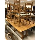 A modern oak dining table raised on twin pedestal supports united by an H stretcher,