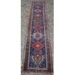 A Persian runner with repeating lozenge medallion decoration on a red ground,