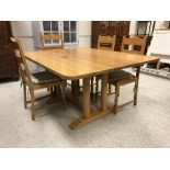 A modern oak dining table raised on twin pedestal supports united by an H stretcher,