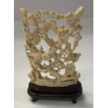 An early 20th Century carved ivory ornament depicting figures in landscape on stand,