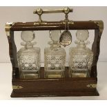 An early 20th Century oak three bottle tantalus containing three hobnail cut bottles,