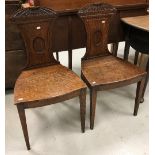 A pair of early 19th Century oak panel seated hall chairs with sunflower style carved top rail over