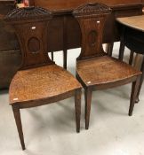 A pair of early 19th Century oak panel seated hall chairs with sunflower style carved top rail over