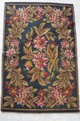 An English needlework rug with centre medallion of floral spray within a floral wreath border,