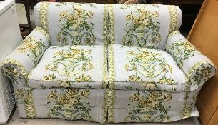 An early 20th Century upholstered two seat sofa on bun feet and castors with loose covers in Jean