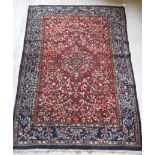 A Persian rug with centre medallion on a floral and foliate decorated red ground,