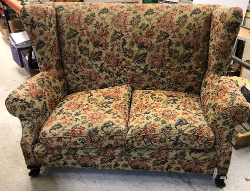 An early 20th Century upholstered wing back scroll arm two seat sofa on squat cabriole legs to claw