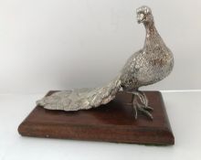 A white metal figure of a peacock set on an oak base,