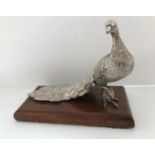 A white metal figure of a peacock set on an oak base,